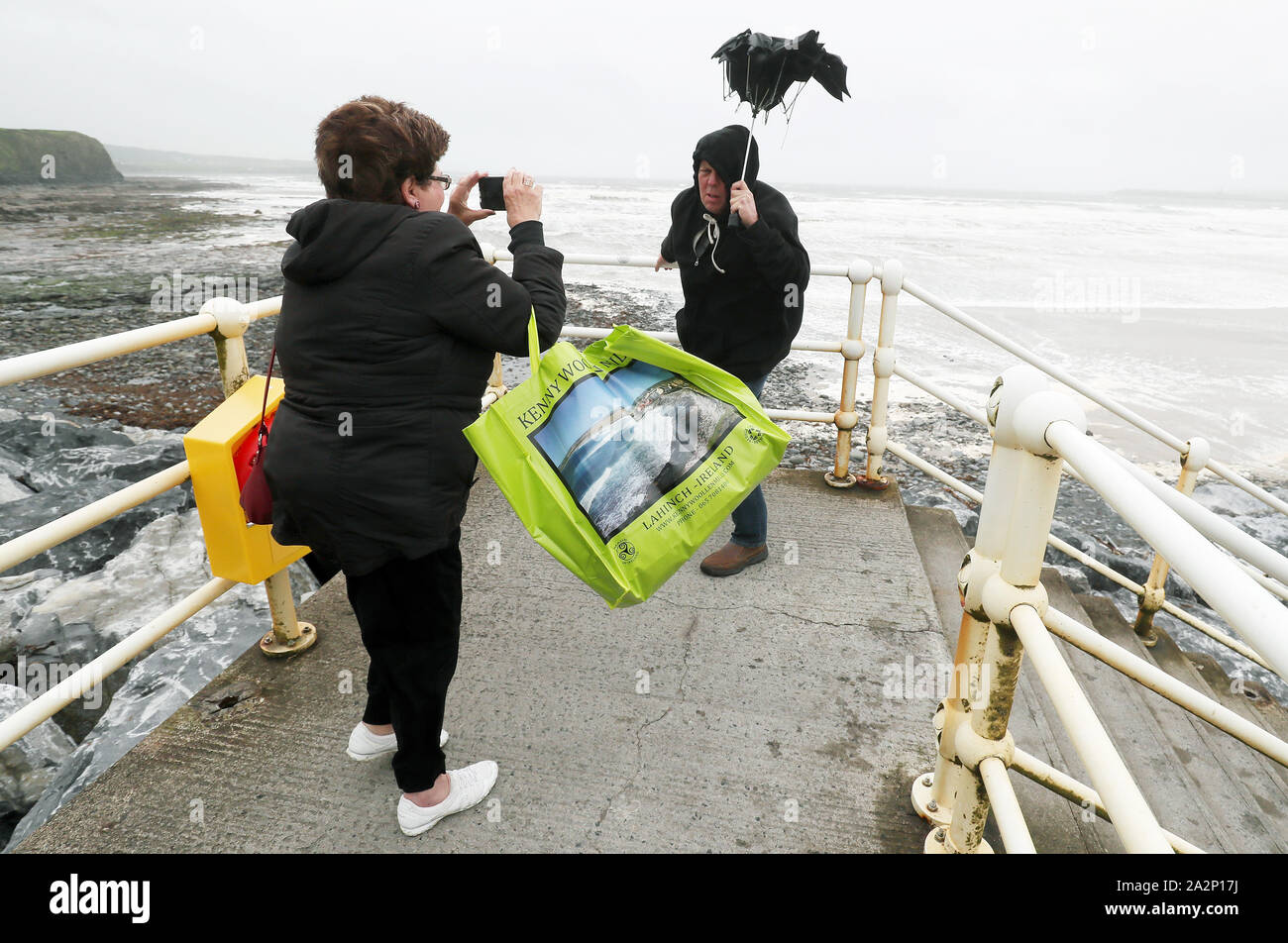 American tourists take photos with a broken umbrella along the sea front in Lahinch, County Clare, on the West Coast of Ireland as storm Lorenzo makes landfall, with a status orange wind warning and a yellow rain warning having been issued. Stock Photo