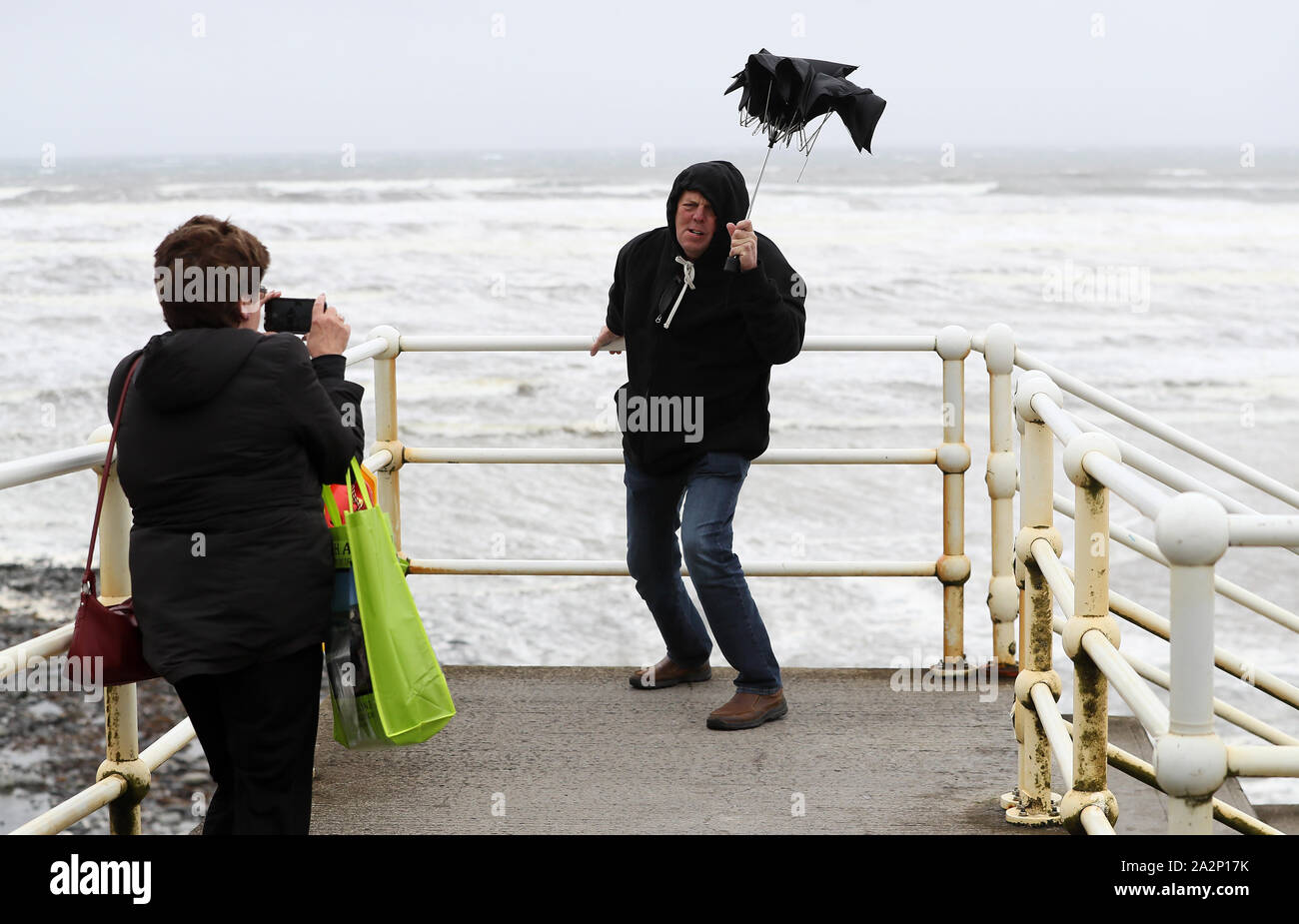 American tourists take photos with a broken umbrella along the sea front in Lahinch, County Clare, on the West Coast of Ireland as storm Lorenzo makes landfall, with a status orange wind warning and a yellow rain warning having been issued. Stock Photo