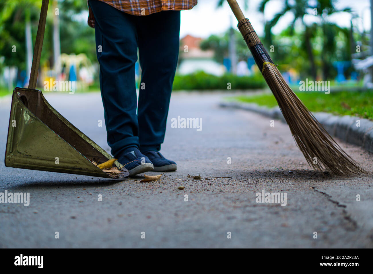 An Asian woman is sweeping dry leaves by the road in the outdoor garden