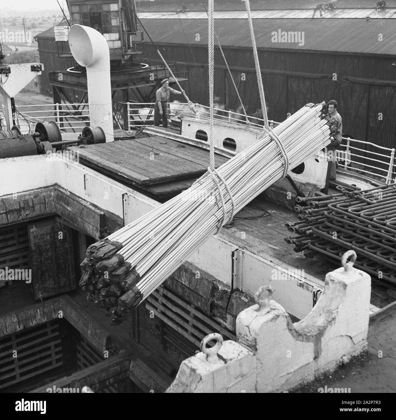 1950s, historical, London Docks, a load of steel pipes for export being lowered into the hull of a steamship moored dockside. Stock Photo
