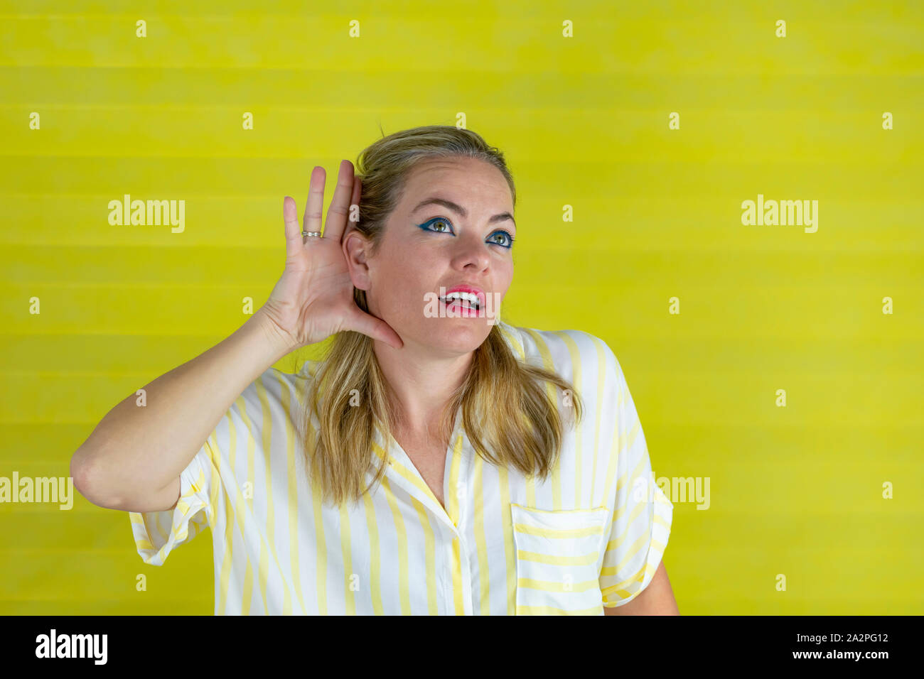 Young woman in fashionable striped shirt smiling with hand over ear listening . Concept of listening. - Image Stock Photo