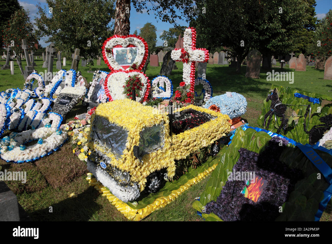 A much decorated grave with a floral Ford lorry in the foreground Stock Photo