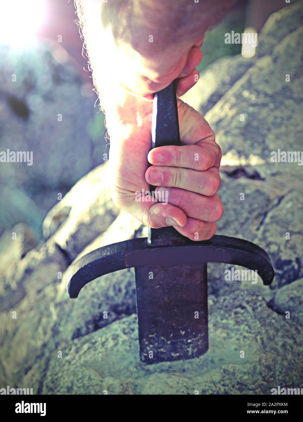 hand of man and the Excalibur Sword in the stone with spotlight Stock Photo