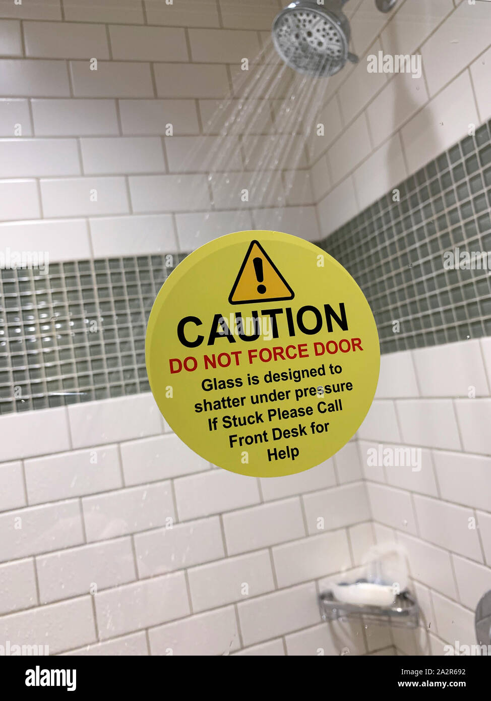 Warning sticker on glass bathroom shower door warning of danger of