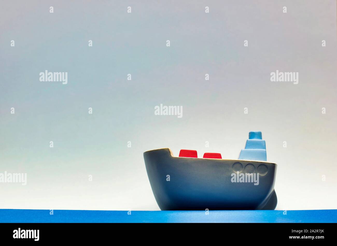 A gray toy cargo ship cruising on water sitting low in the frame, with open sky in the background with room for text above. Stock Photo