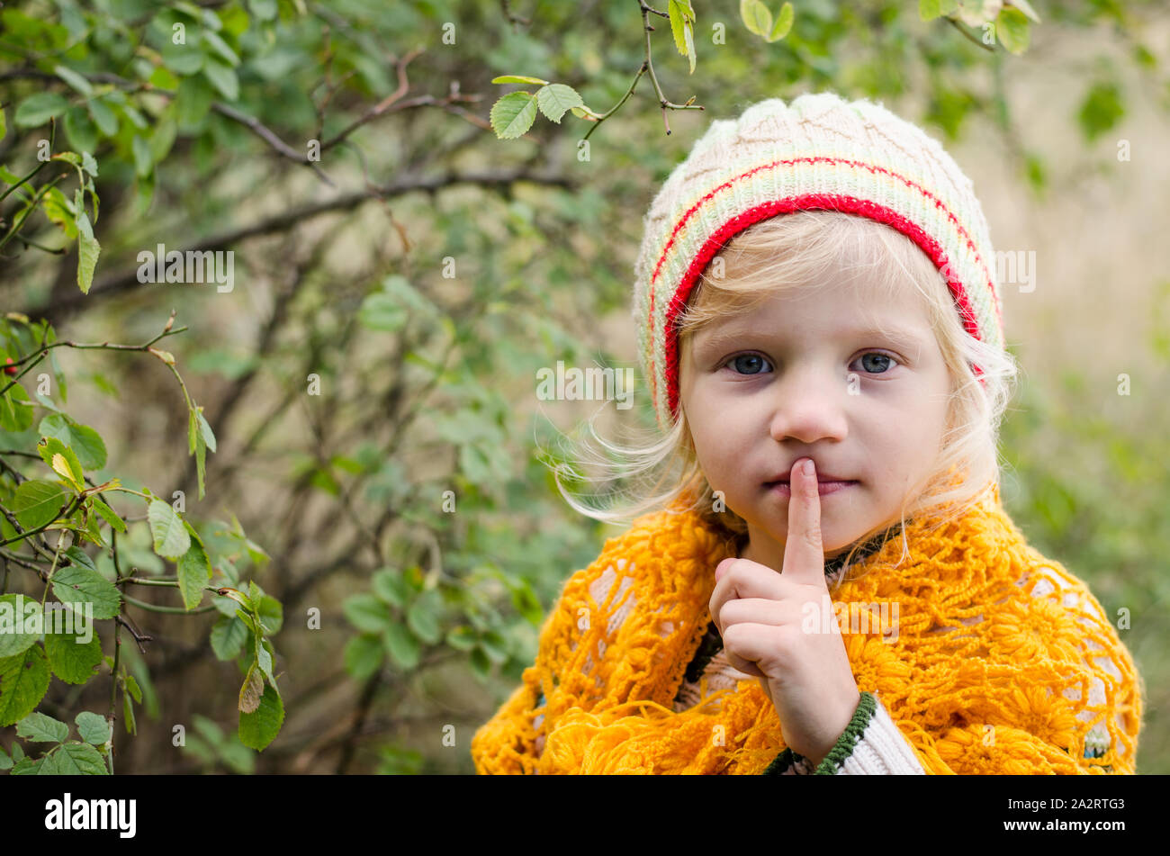 beautiful little blond girl in cap making silence geture, pst..... Stock Photo