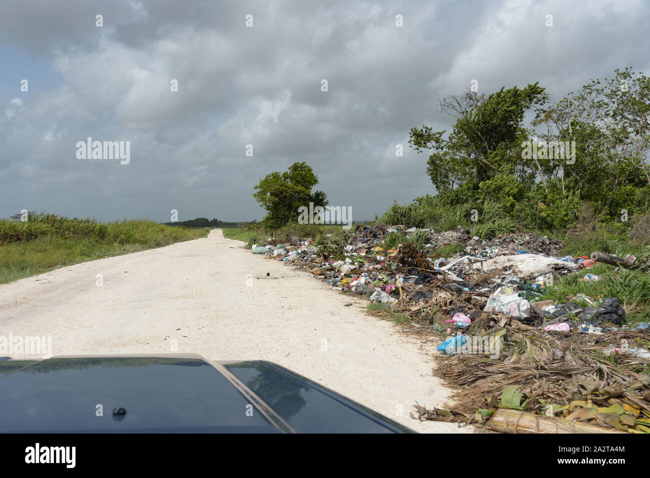 Orange Walk, Belize - May 21, 2017: Trash dumped next to road - highlights the issue of roadside garbage disposal in Latin America. View through winds Stock Photo