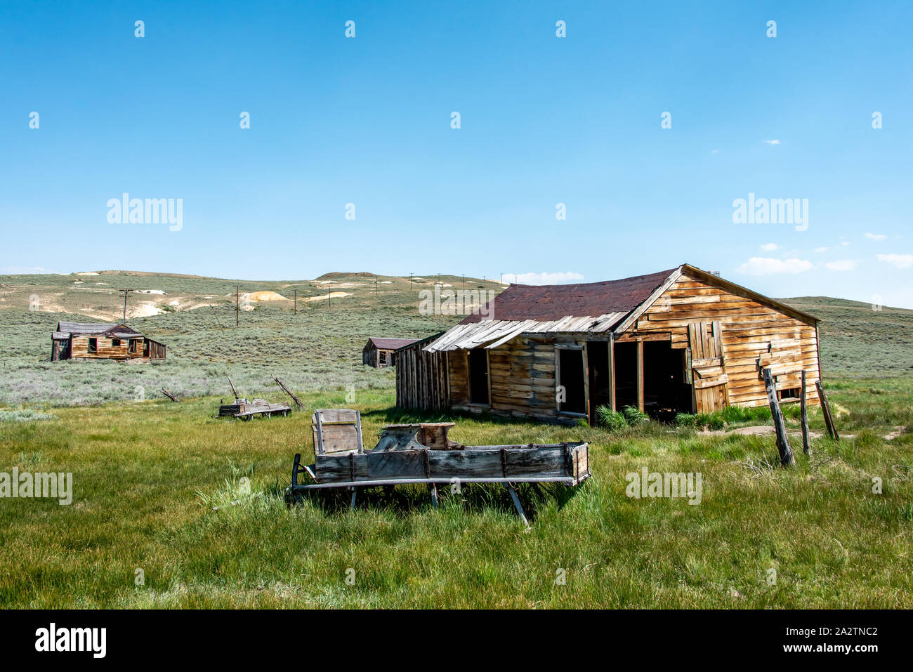 A wooden buckboard or wagon sits abandoned in grass outside a decrepit house or barn at Bodie State Historic Park, a ghost town in California. Stock Photo