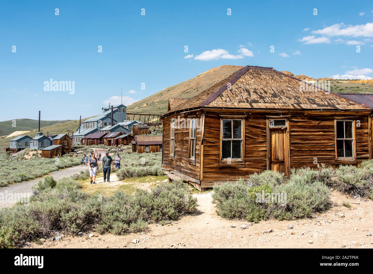 People explore Bodie State Historic Park with the Standard Consolidated Mining Company Stamp Mill in the background and an old wooden house beside the Stock Photo