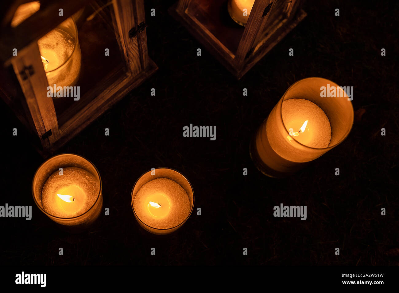 Many burning candles in glass and wooden lanterns on dark ground outdoor at night. Romantic party area. Diwali fire holiday Stock Photo