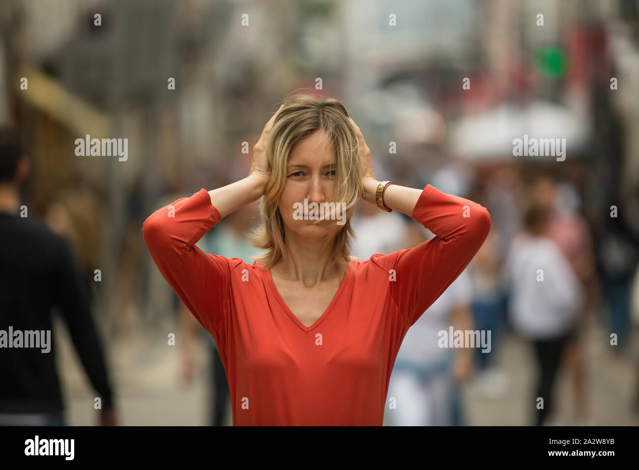 Panic attack in the street. Woman covers his ears with hands at standing in the middle of a busy street. Stock Photo