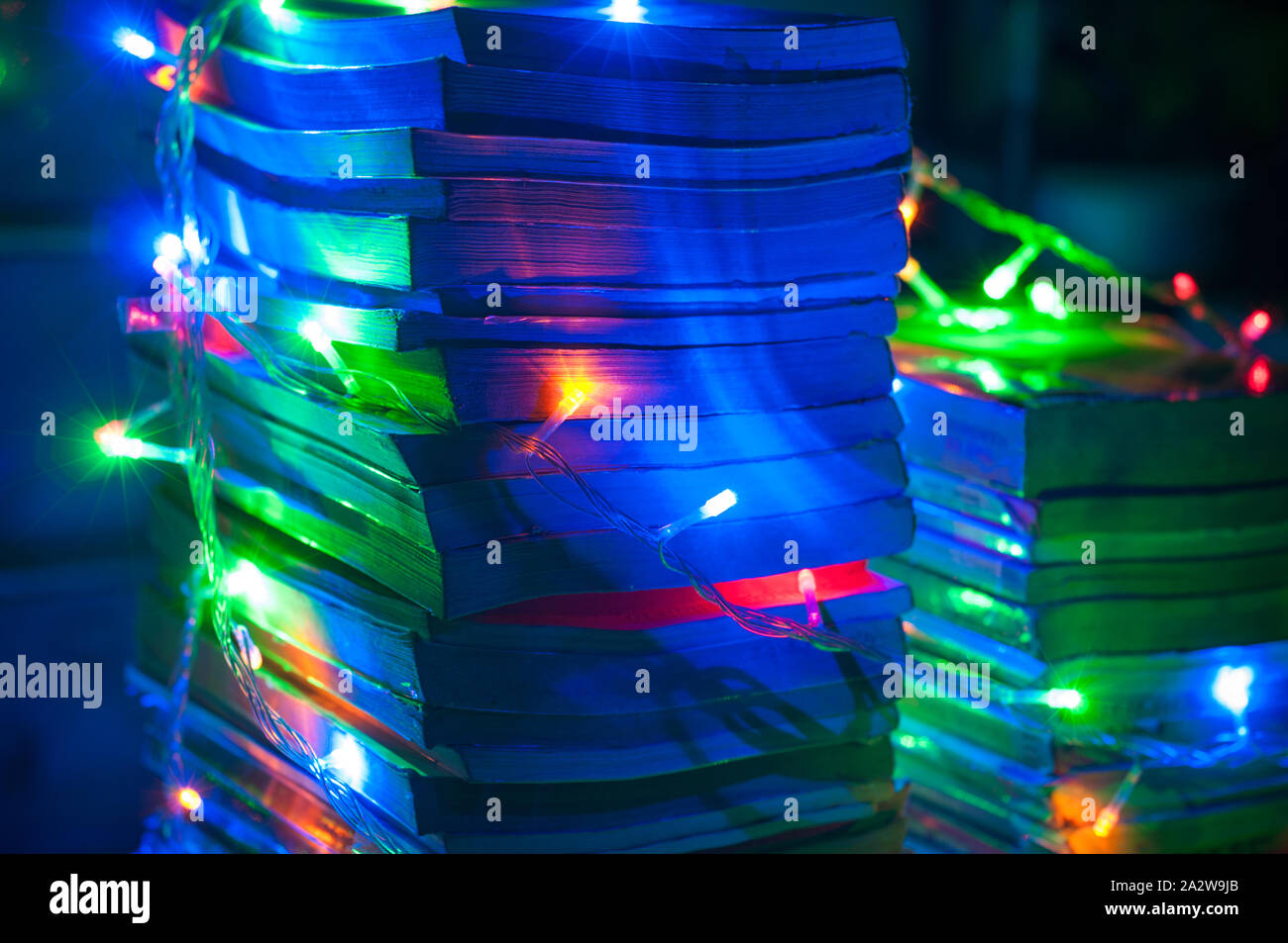 Christmas light coiled all around on a tower of books. String lights. Close up shot of book compilations. Blue wallpaper. Stock Photo