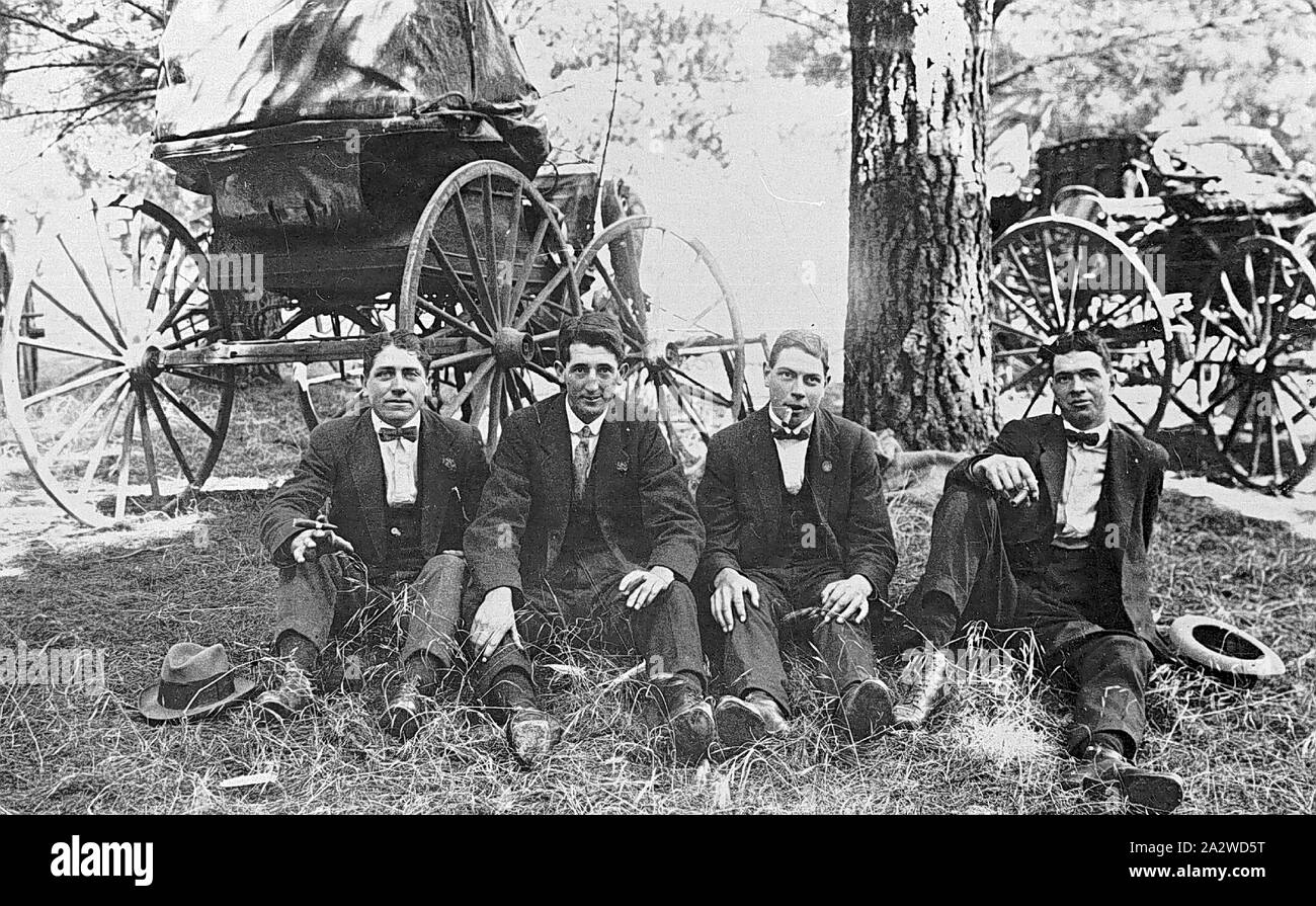 Negative - Four Men Smoking Cigars at Trade Picnic, Ballarat District, Victoria, circa 1920, Four men seated on the ground at a trade picnic, they are smoking cigars. There are two buggies in the background Stock Photo