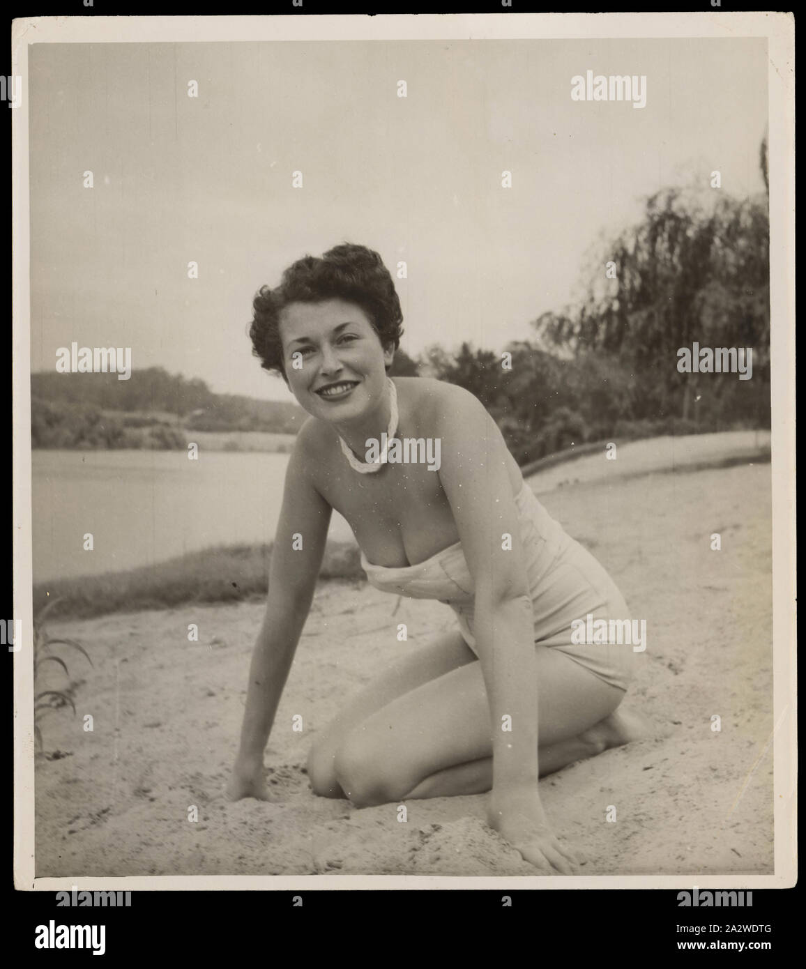 Photograph - Bernice Kopple in Swimsuit Kneeling on Beach, Hawkesbury River, Sydney, Australia, Nov 1953, Photograph of Bernice Kopple in a light-coloured one-piece, strapless swimsuit, kneeling and leaning forward with hands on the sand, on the beach at Hawkesbury River, Sydney, Australia, Nov1953, In the 1950s and 1960s Bernice Kopple worked as a fashion photographic model and as a performer on the Tivoli Circuit. Bernice Kopple was born in Glasgow, Scotland in 1930 and migrated to Melbourne Stock Photo