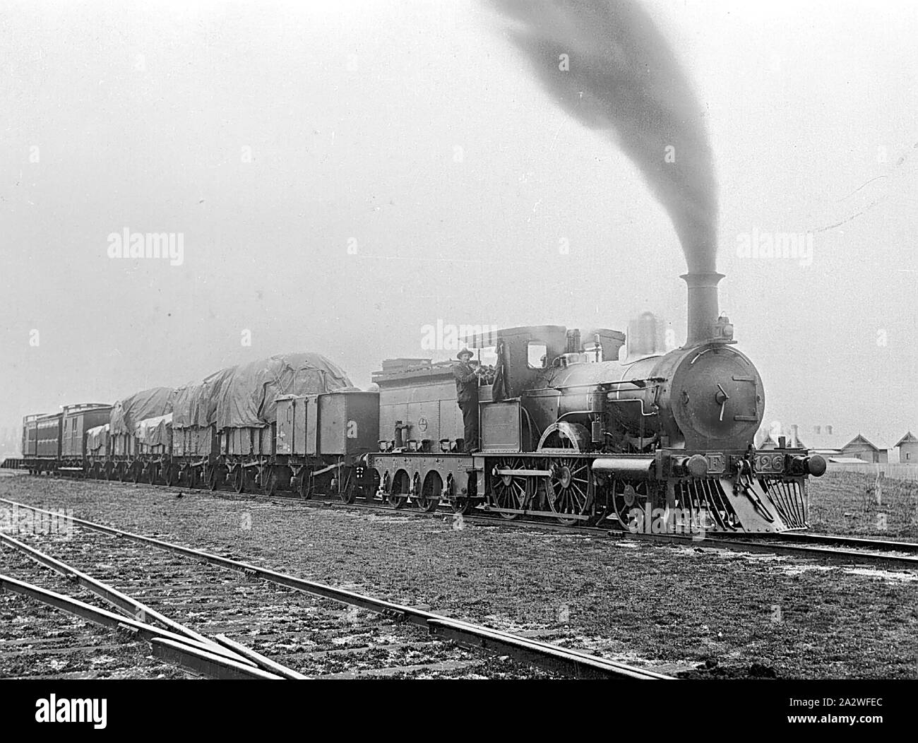 Negative - Victorian Railways F-Class 2-4-0 Steam Locomotive Hauling a Mixed Goods & Passenger Train, Waubra, Victoria, 1910, Copy of a black & white photograph depicting one of the 2-4-0 type steam passenger locomotives built by the Phoenix Foundry, of Ballarat, during the late 1870s, for use on the country branch lines or 'light lines' that were built throughout central Victoria between 1873 and 1893. The engines were built in two batches Nos.126-144 (even numbers only), which went into service in 1876-77 Stock Photo