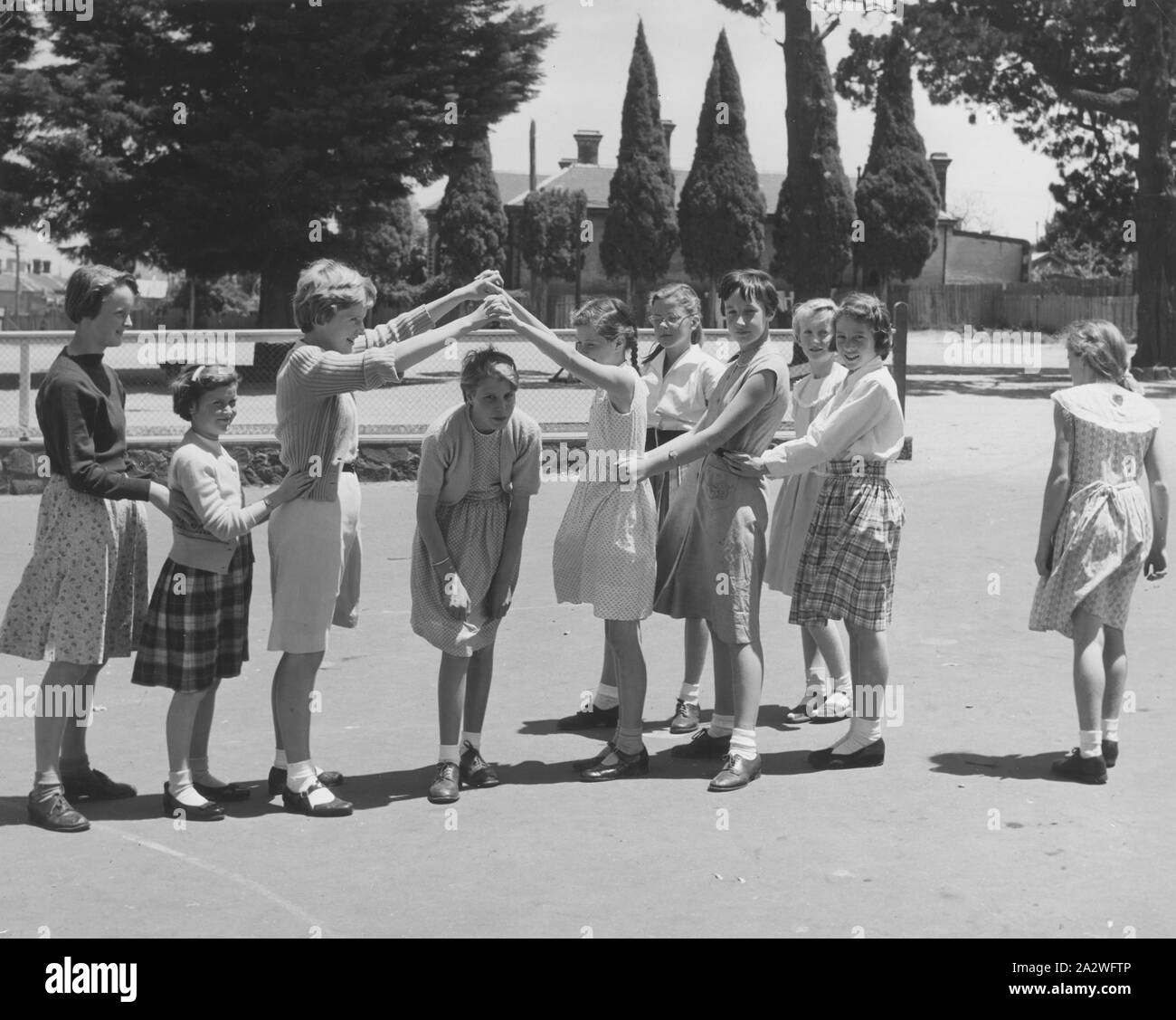 Photograph - Girls Playing 'Oranges & Lemons' Game, Dorothy Howard Tour, Melbourne, 1954, Black and white photograph depicting 10 girls playing 'Oranges & Lemons' in a government school playground, Melbourne, Victoria, 1954. It is one of a group of photographs probably taken by American folklorist Dr Dorothy Howard while she was studying children's games and playlore in Australia under a Fulbright research grant,1954-1955. Her photographs and research have become part of Stock Photo