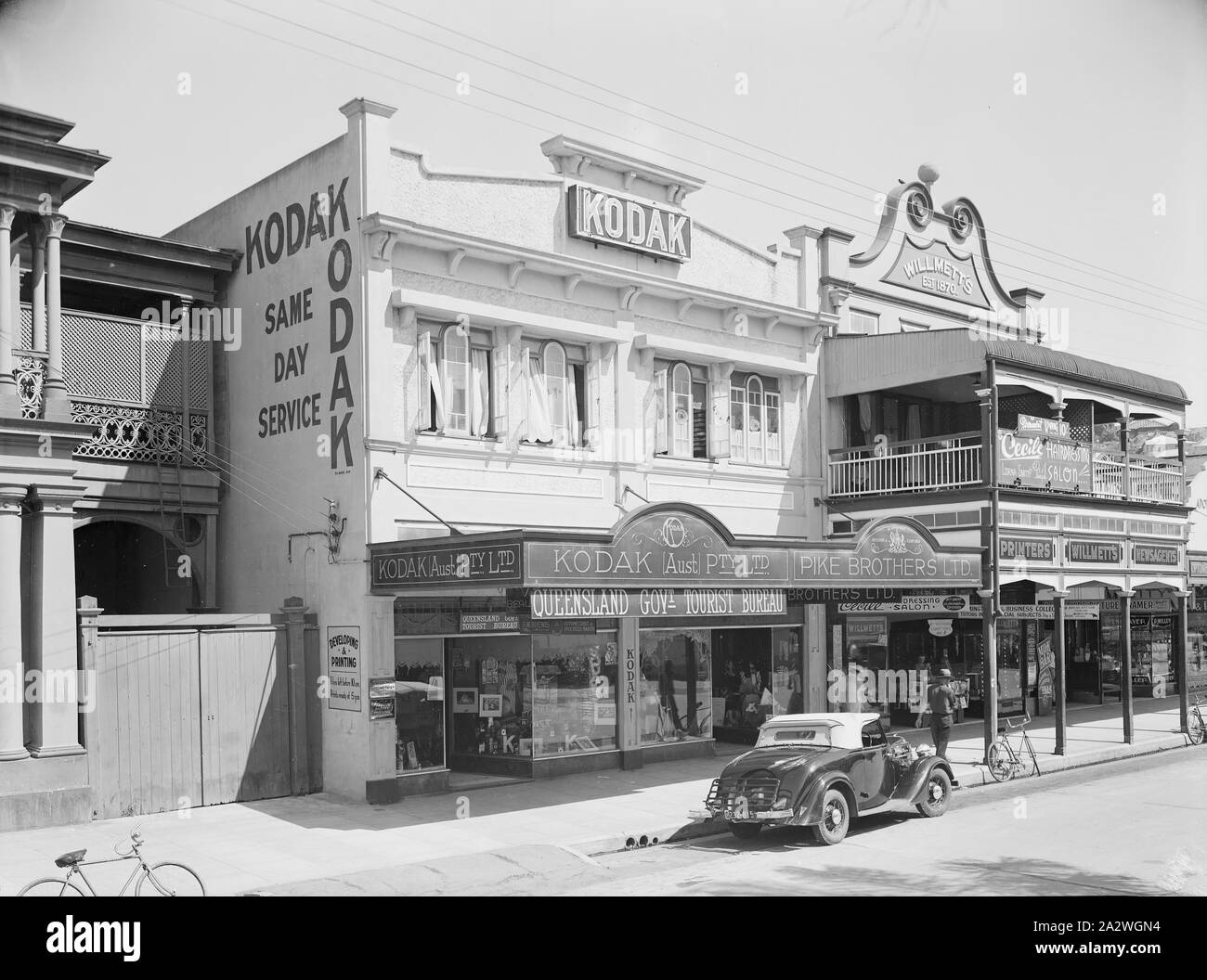 Negative, Shop Exterior Kodak Branch, Townsville, QLD, 1930s, Black and white film negative of the Kodak Australasia Pty Ltd branch store and same day processing laboratory on Flinders St, Townsville, Queensland, in the 1930s. This Kodak store was built in 1920, with the second story added in 1929. Upstairs was the processing lab for printing and developing, and downstairs was the retail shop. Out the back there was a dense tropical garden, shared by Kodak Stock Photo