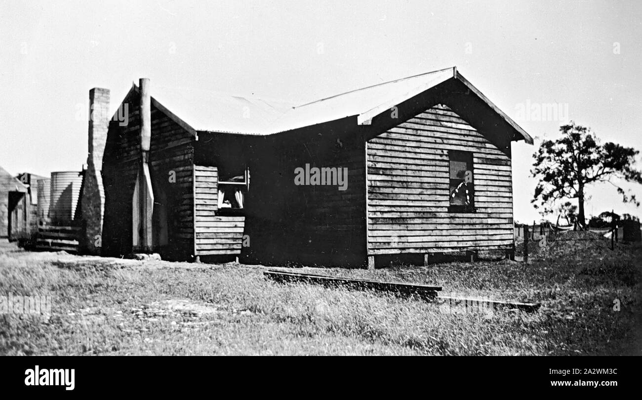 Negative - Dilapidated House With Two Chimneys & Water Tank, Cavendish District, Victoria, circa 1935, A dilapidated house. There are two chimneys on one wall and a water tank in the background. Two large windows are visible, one is open and the curtains can be seen. The house appears to be Victorian timber. There is a large tree in the background and a wire fence Stock Photo