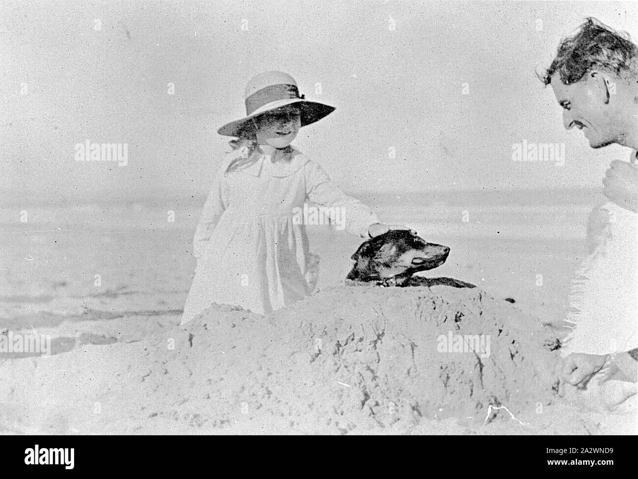 Negative - Girl Petting a Dog on the Beach, Lorne, Victoria, 1920, A young girl appearing to bury a dog in the sand. (He is either a very good natured dog or it is a trick photograph with the dog behind the sand mound Stock Photo