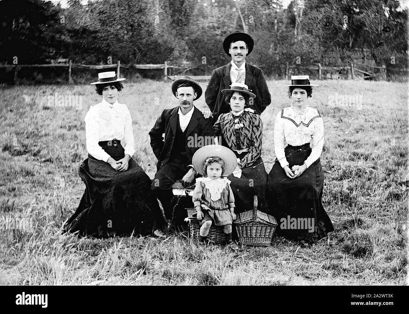 Negative - Picnic, Victoria, circa 1905, Two men, three women and a small child at a picnic in a field. There are two picnic baskets and the child is seated on one of them. There is a strong facial resemblance between the three women - they are, presumably, sisters Stock Photo