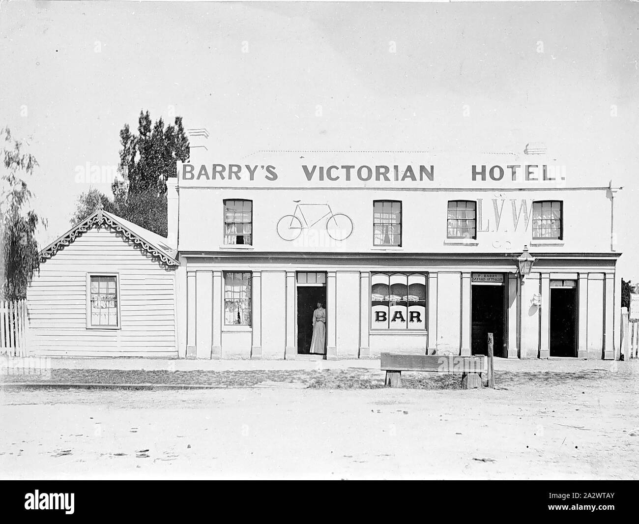 Negative - Gisborne, Victoria, 1899, Barry's Victorian Hotel. A woman stands in the doorway and there is a bicycle drawn on the wall of the hotel and the letters 'LVW Stock Photo