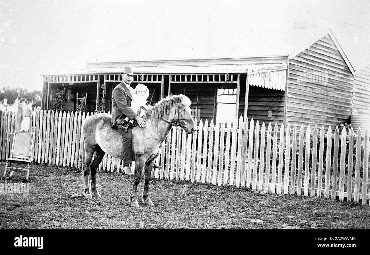 Negative - Maffra, Victoria, 1916, A man on horseback. He is riding without a saddle and holds a small child in front of him. There is a wooden house behind them Stock Photo
