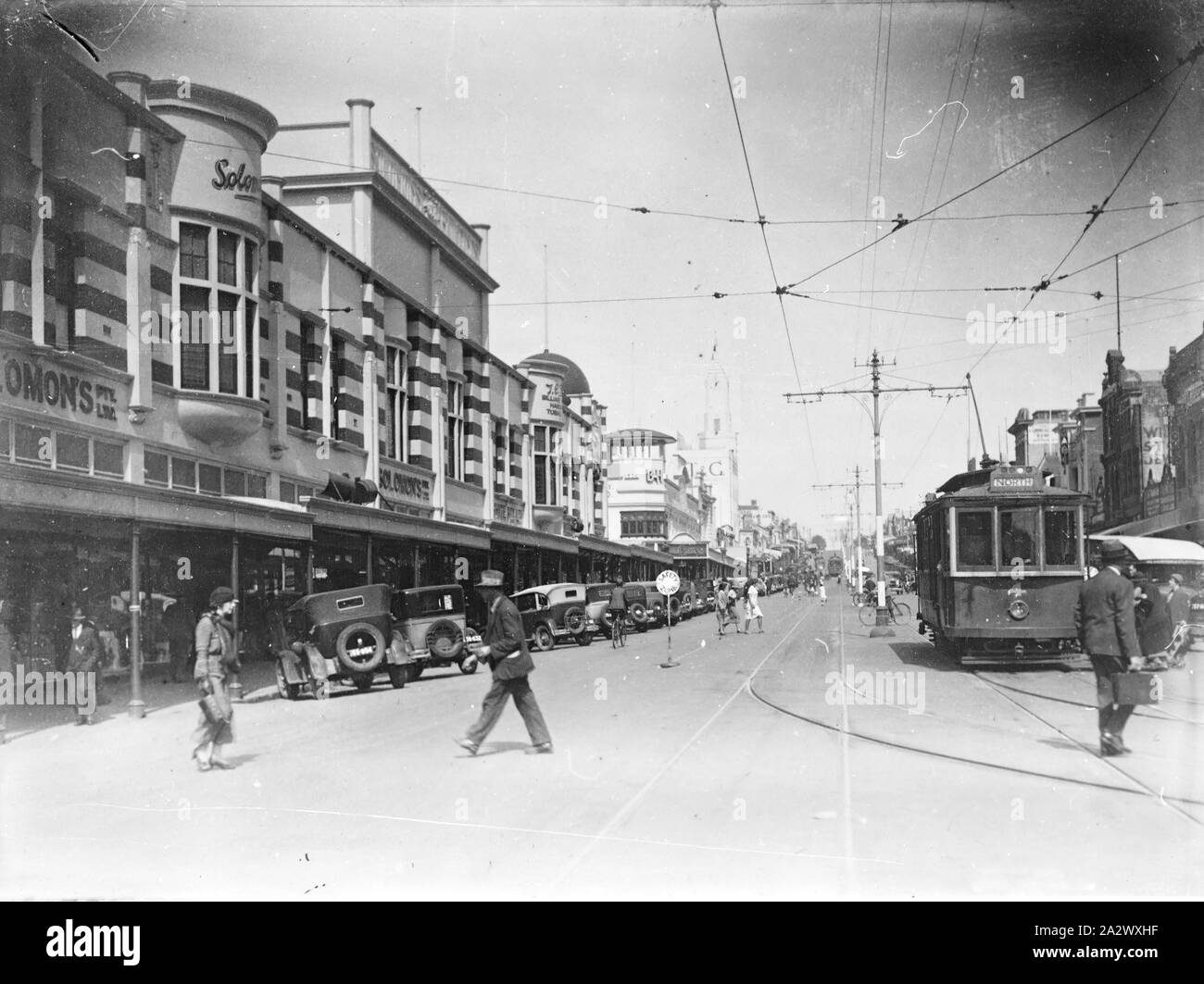 Negative - Moorabool Street, Geelong, Victoria, circa 1935, Black and white negative of Moorabool Street, viewed from Malop Street, Geelong, circa 1935. The streetscape shows pedestrians, trams and motor cars. The cars are parked along the street in front of Solomon's Building, a popular shopping emporium. Originally built in 1912-1913, in the mid 1980s Solomon's Building became part of the Market Square shopping development, with only the facade Stock Photo