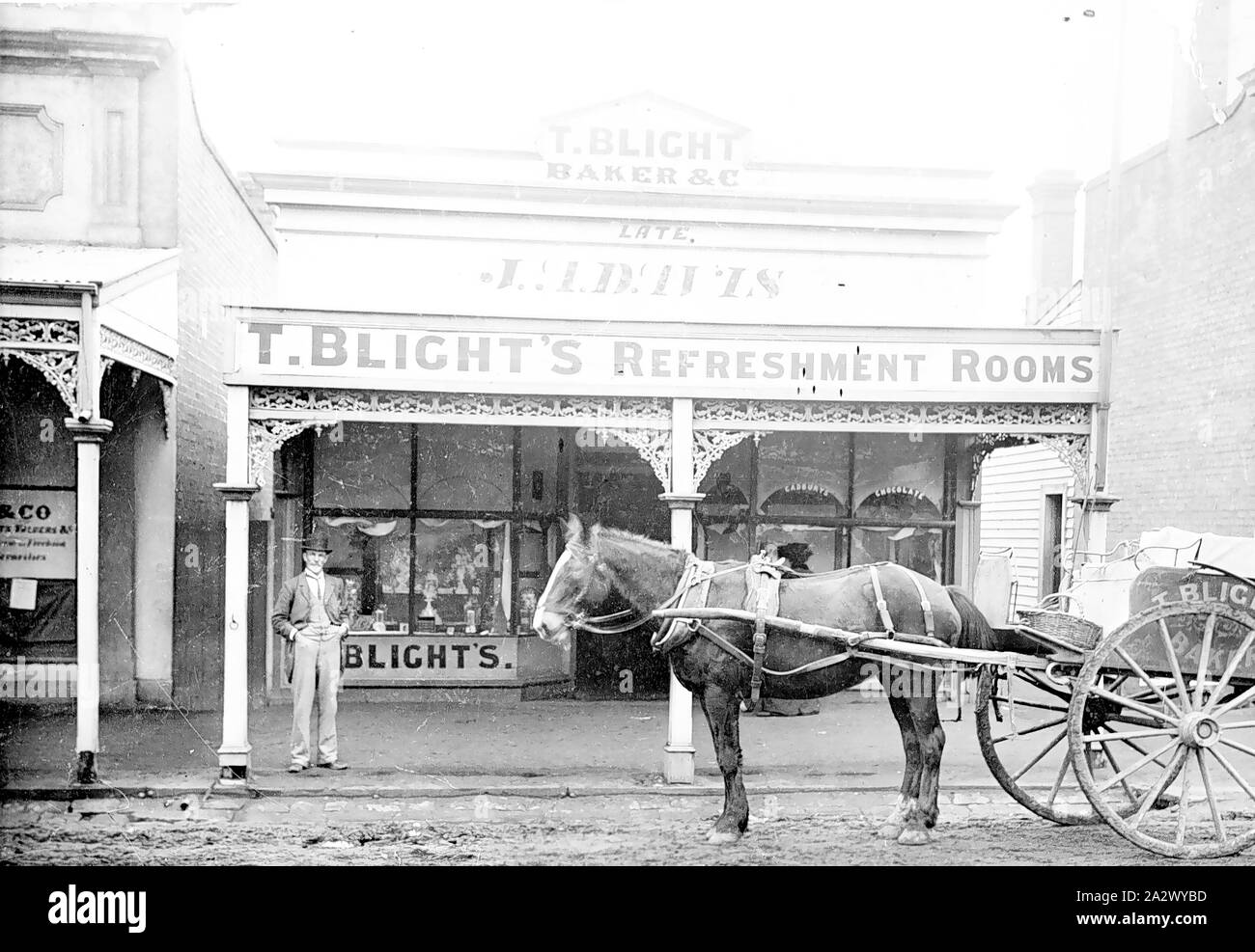 Negative - Horsham, Victoria, circa 1895, Thomas Blight standing in front of his refreshment rooms. There is a horse-drawn delivery cart in front of the building with the name Blight on it. The front windows are dressed for display Stock Photo