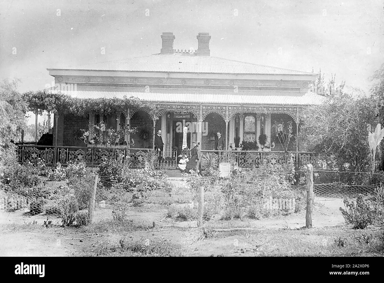 Negative - Bendigo District (?), Victoria, circa 1905, A family on the verandah of their home. The house is brick with iron lacework and there is a vine growing along the verandah. The front and back doors are open allowing a view through the house to the back yard Stock Photo