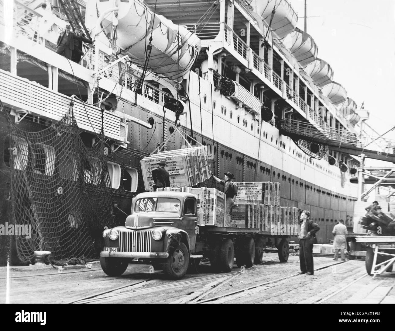 Photograph - H.V. McKay Massey Harris, Orontes Being Loaded with Food Parcels, Port Melbourne, Victoria, Dec 1948, Black and white photograph of the ship 'Orontes' being loaded with food parcels from a Ford truck for the 'Food for British Workers Appeal'. Photograph is located in an album: Volume No. 10: Portraits, Sundry Machines, Royal Show 1945-51, page 135. This is one of 25 albums that provide detailed visual documentation of the activities of the McKay enterprise. This image forms part of Stock Photo