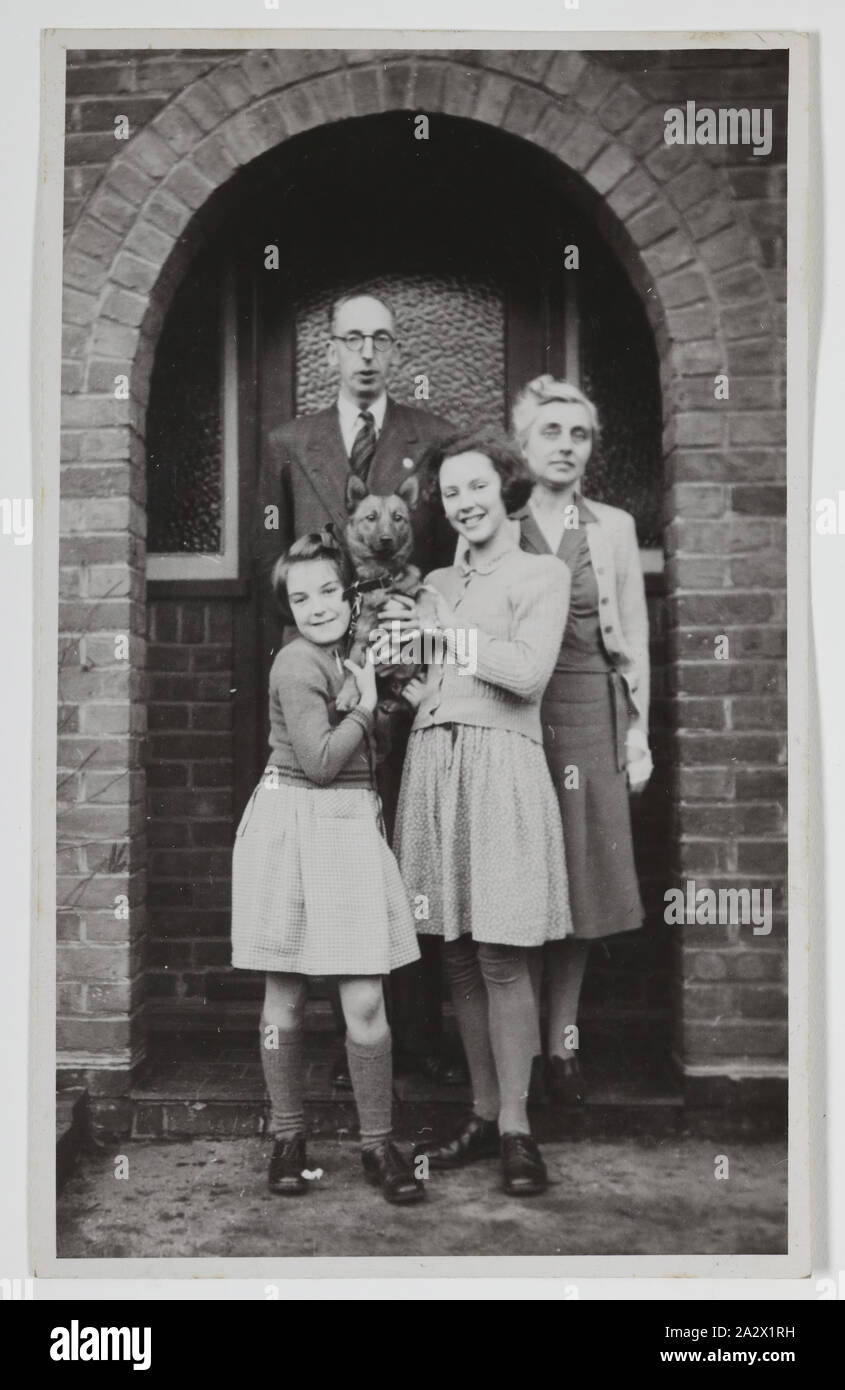 Photograph - Palmer Family Outside House, Iver, England, circa 1947, Black and white photograph of George and Gertrude Palmer and their daughters Shirley and Lesley, and their dog Robbie, in England around 1947. It was probably taken at George's sister's house in Iver, Buckinghamshire by George's brother-in-law David Roberts, the day before they left for Australia. It was brought to Australia by George Palmer when he migrated to Australia from England with his wife Stock Photo