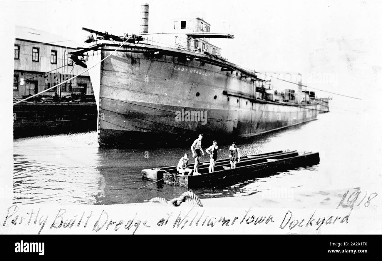 Negative - Williamstown, Victoria, 1918, The 'Lady Stanley', a partly built dredge at the Williamstown dockyard there is a group of men in bathing costumes on a barge in the foreground Stock Photo
