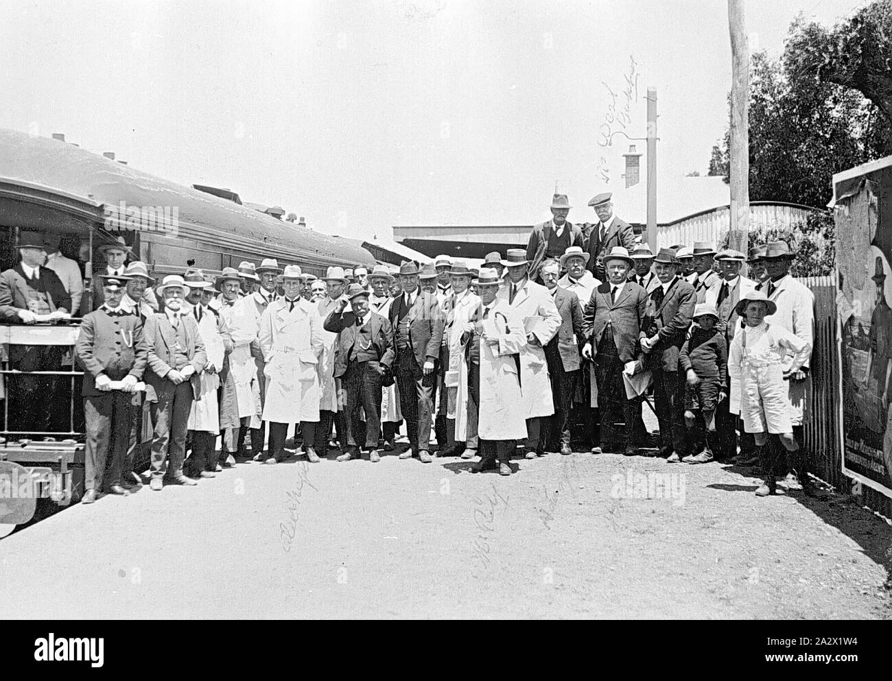 Negative - Rainbow, Victoria, 1925, A large group of people gathered on the platform of Rainbow Railway Station for the visit of the Better Farming Train. Many men are wearing suits, and some wear white coats (possibly 'labcoats') over their clothes. A man standing on the far left is wearing station staff uniform. An advertising poster is mounted on the platform fence Stock Photo