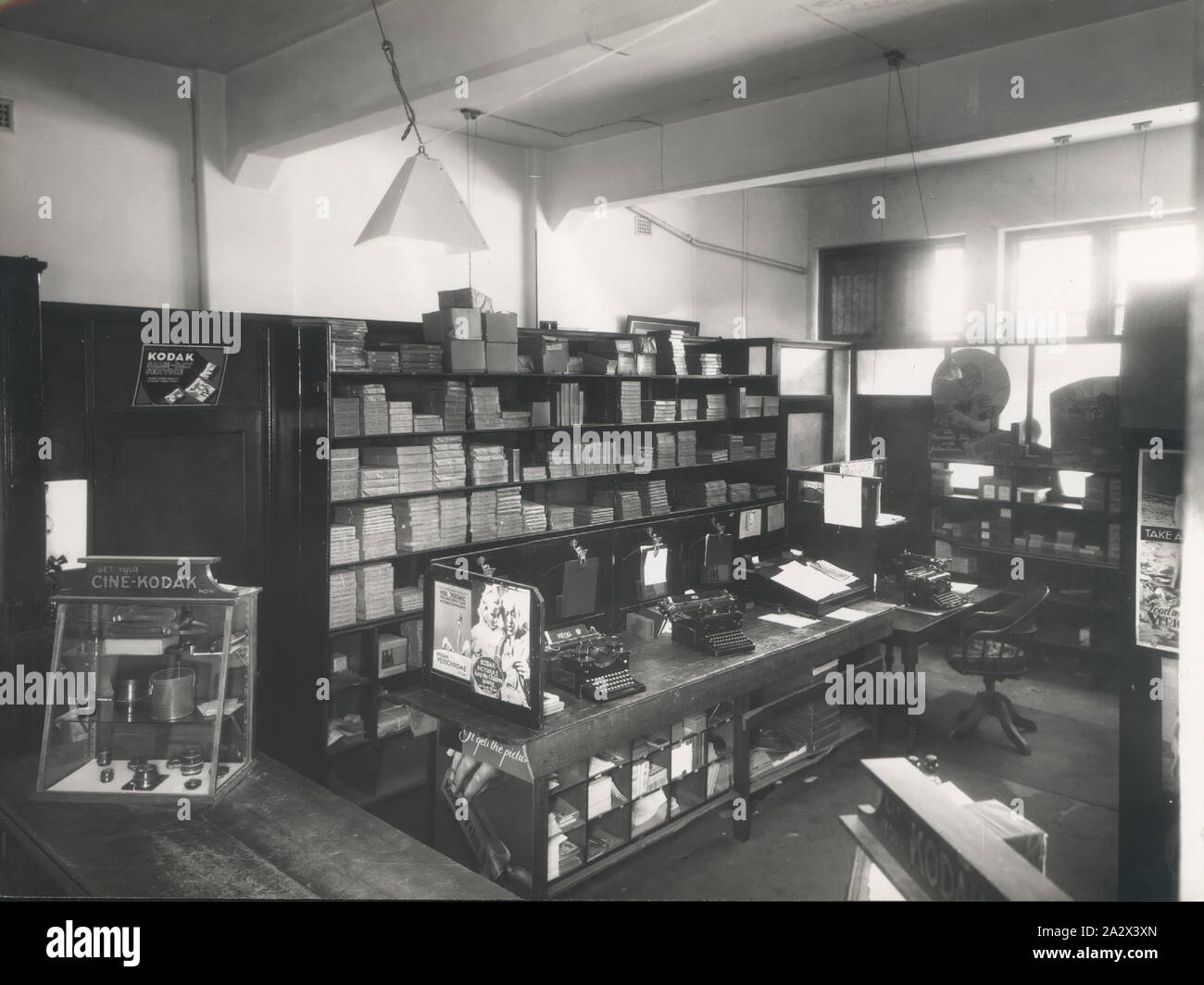 Photograph, Shop Interior, Perth, Western Australia, 1935, Black and white photograph of the Kodak Australasia Pty Ltd shop interior at 662 Hay Street, Perth. It features the working area behind the front counter, including a workstation with two typewriters, a shelf full of photographic paper and film products, various glass fronted retail cabinets and a window leading outside. This is one of 3 photographs of the Perth facilities, printed at Stock Photo