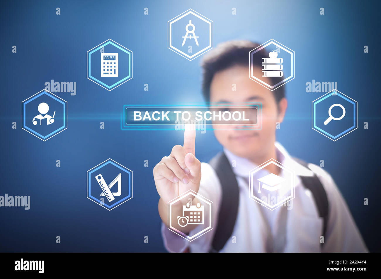 School boy wearing in school uniform and back pack bag pressing the button Back to school using hologram on isolated blue background Stock Photo