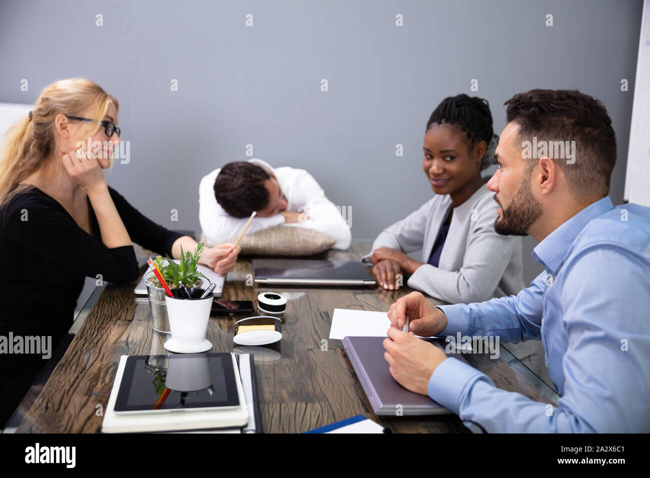 Tired Businessman Sleeping On Office Desk While His Colleagues Discussing In Meeting Stock Photo