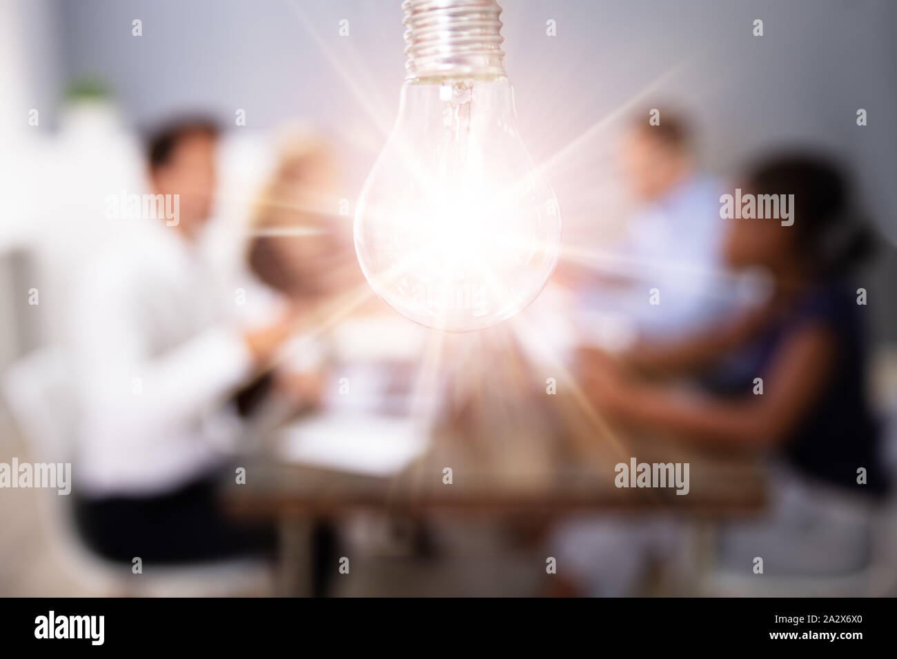 Lightbulb On In Front Of People In Creative Meeting Stock Photo