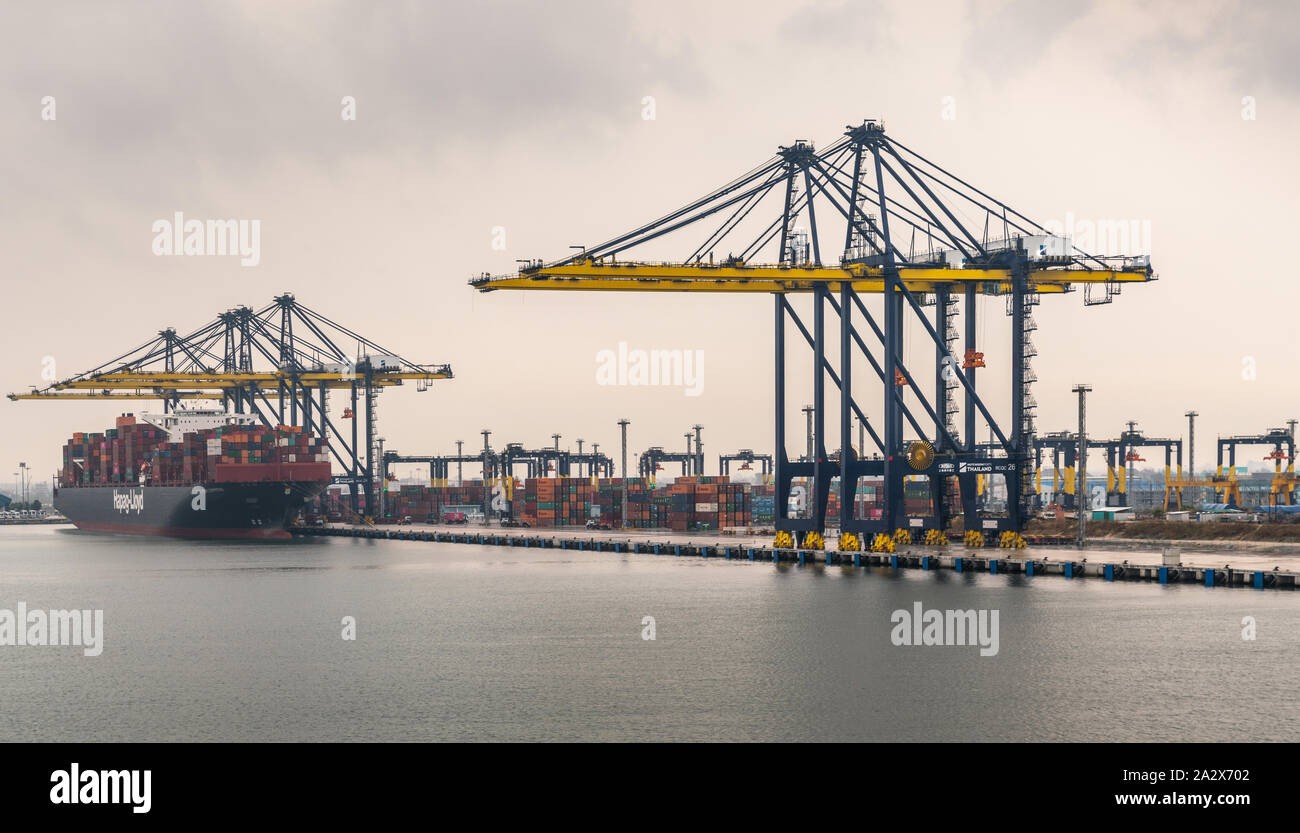 Laem Chabang, Thailand - March 16, 2019: Entering Container port and terminal from the sea under gray cloudscape. Yellow cranes and Hapag Lloyd ship o Stock Photo
