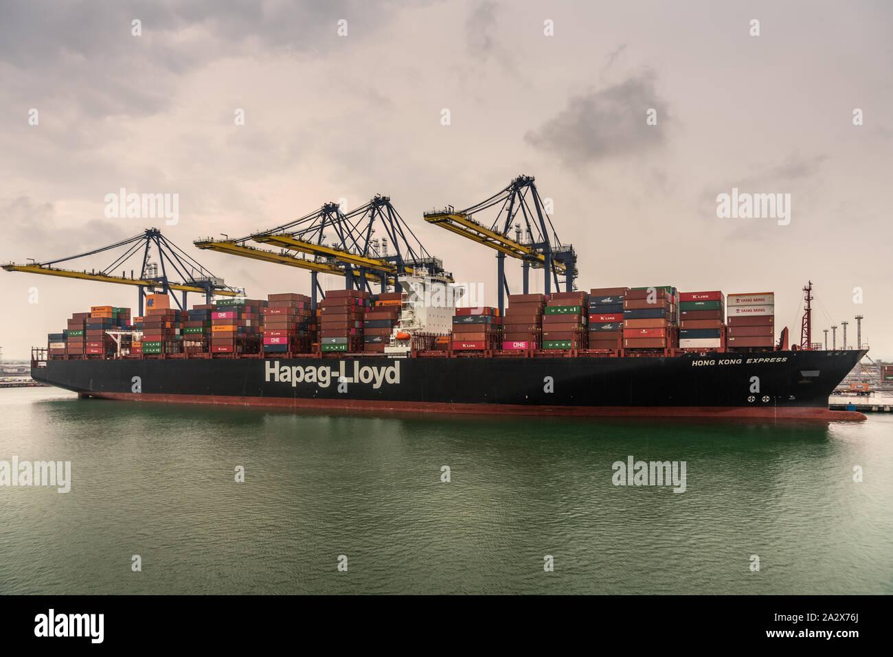 Laem Chabang, Thailand - March 16, 2019: Container port and terminal and Hapag Lloyd ship under gray sky. Four yellow cranes loading and unloading it. Stock Photo