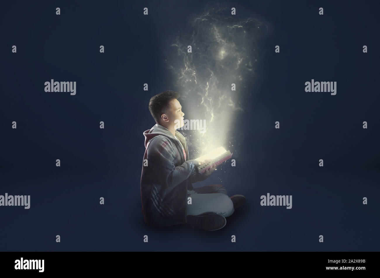 A school boy wearing a jacket holding and reading a magical book with mystical light coming out. Ideas from reading. Depicting education. Stock Photo