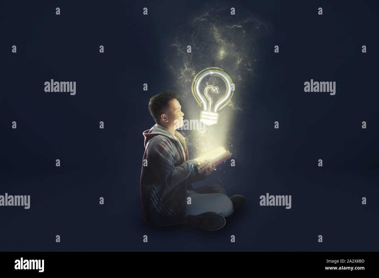 A school boy wearing a jacket holding and reading a magical book with Light Bulb coming out. Ideas from reading. Stock Photo