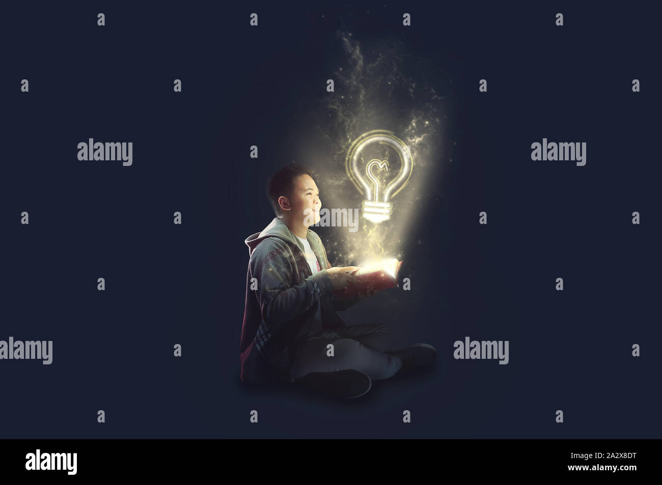 A school boy wearing a jacket holding and reading a magical book with mystical light coming out. Ideas from reading. Depicting education. Stock Photo