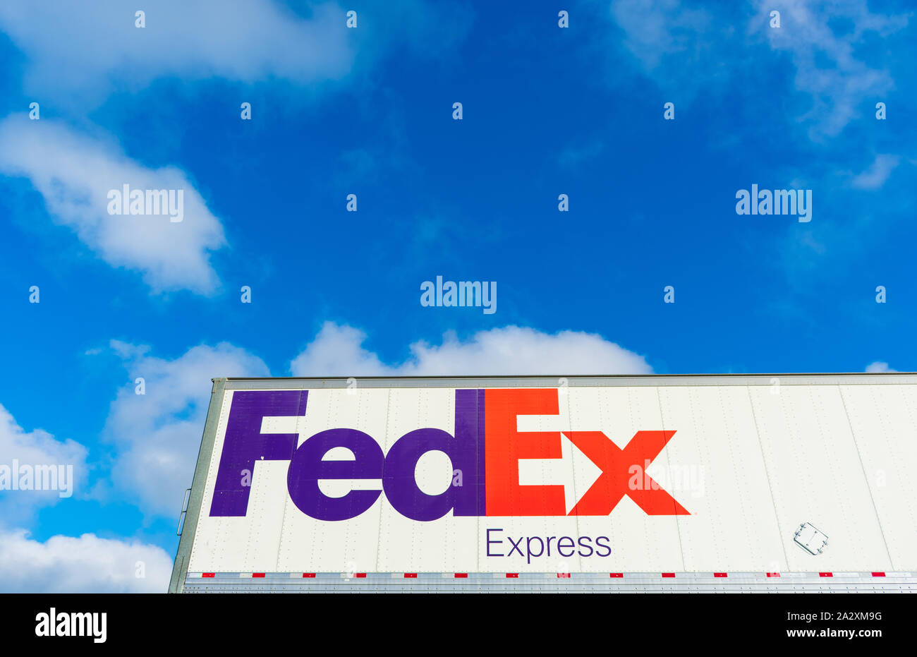 FedEx Express sign on the side of FedEx Corporation delivery truck parked outdoors under blue sky with light clouds Stock Photo