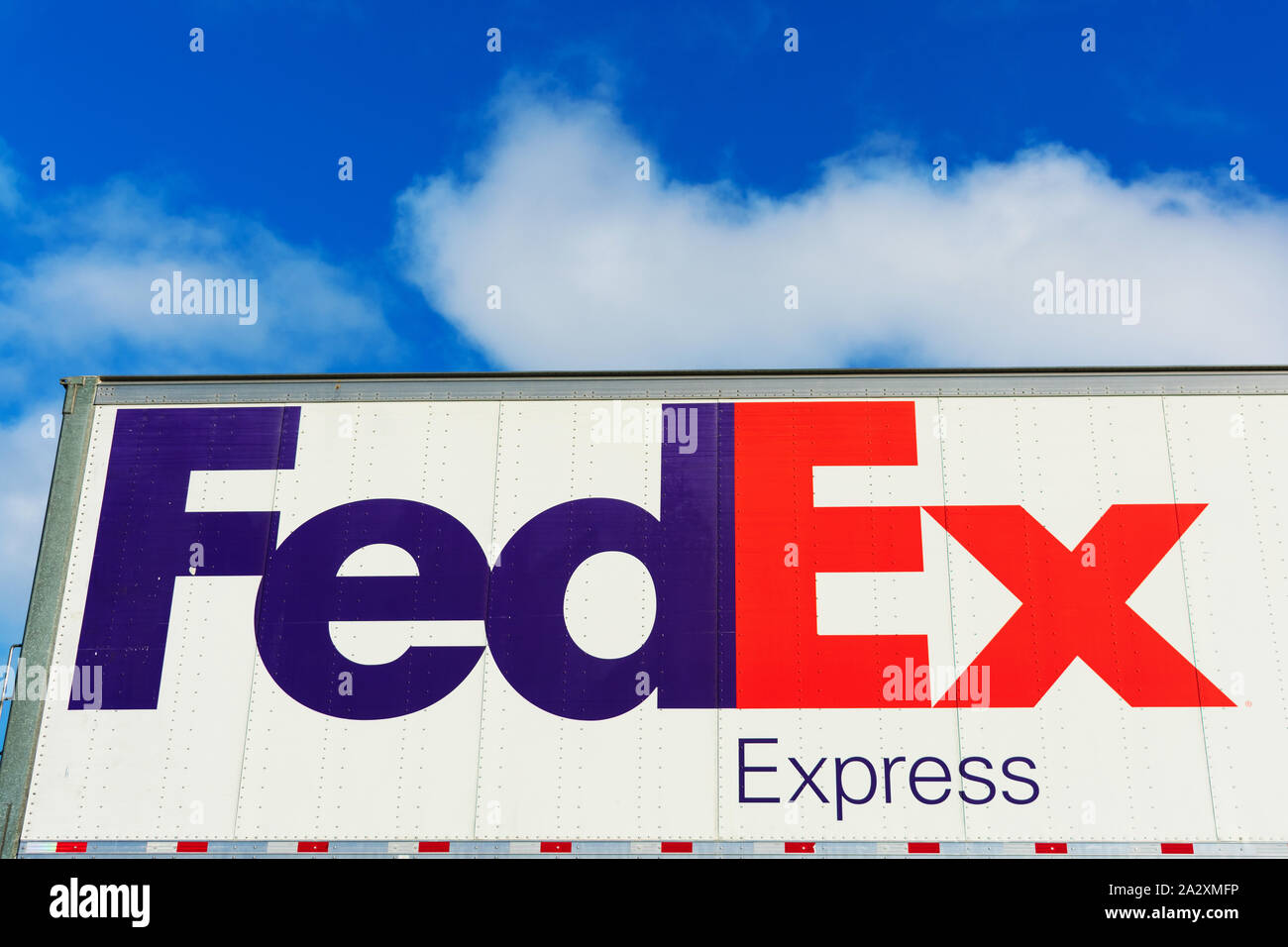 FedEx Express sign on the side of FedEx Corporation delivery truck parked outdoors under blue sky with light clouds Stock Photo