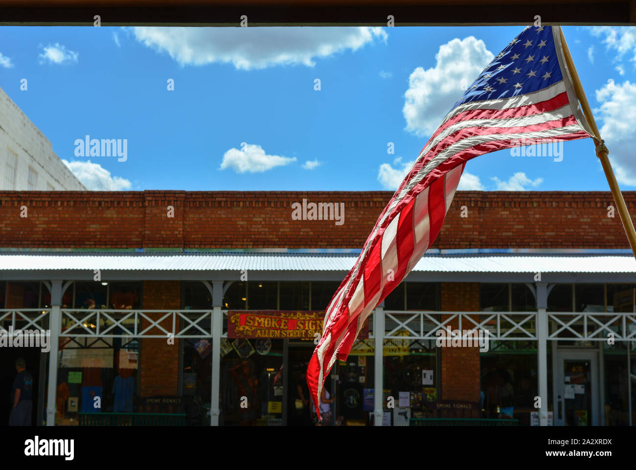 Large American flag flies over old brick buildings along the storefronts in the legendary and historical small town America West site of Tombstone, AZ Stock Photo