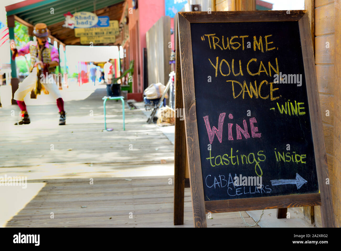 Sandwich board sign promoting wine merchant has funny quote while street dancing performer nearby on the wooden sidewalks of legendary Tombstone, AZ, Stock Photo
