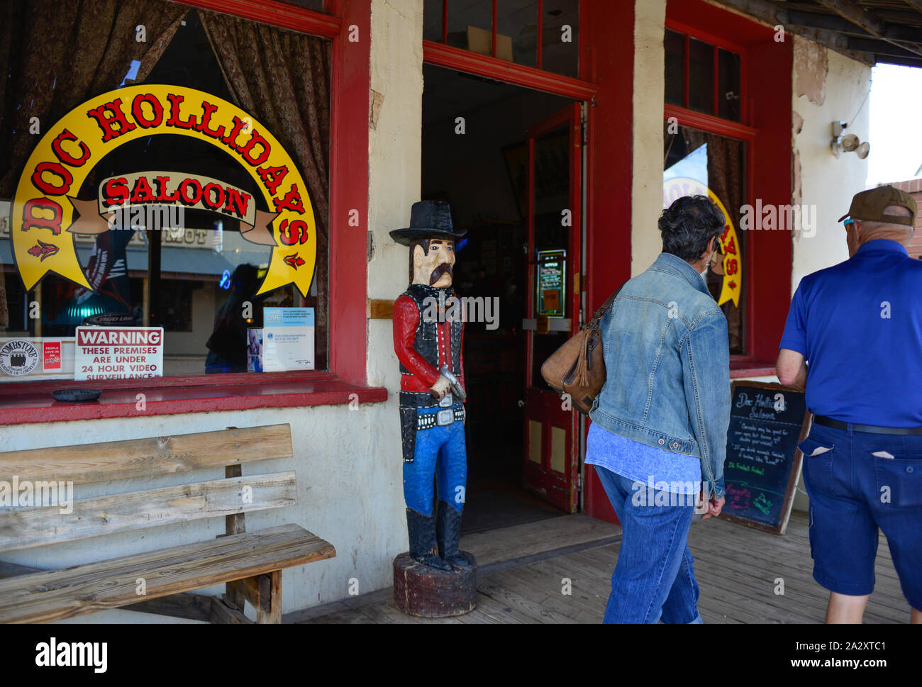 Entrance to Doc Holliday's Saloon with wooden cowboy statue greeting tourists as they stroll the storefronts in Old Western town of Tombstone, AZ, USA Stock Photo