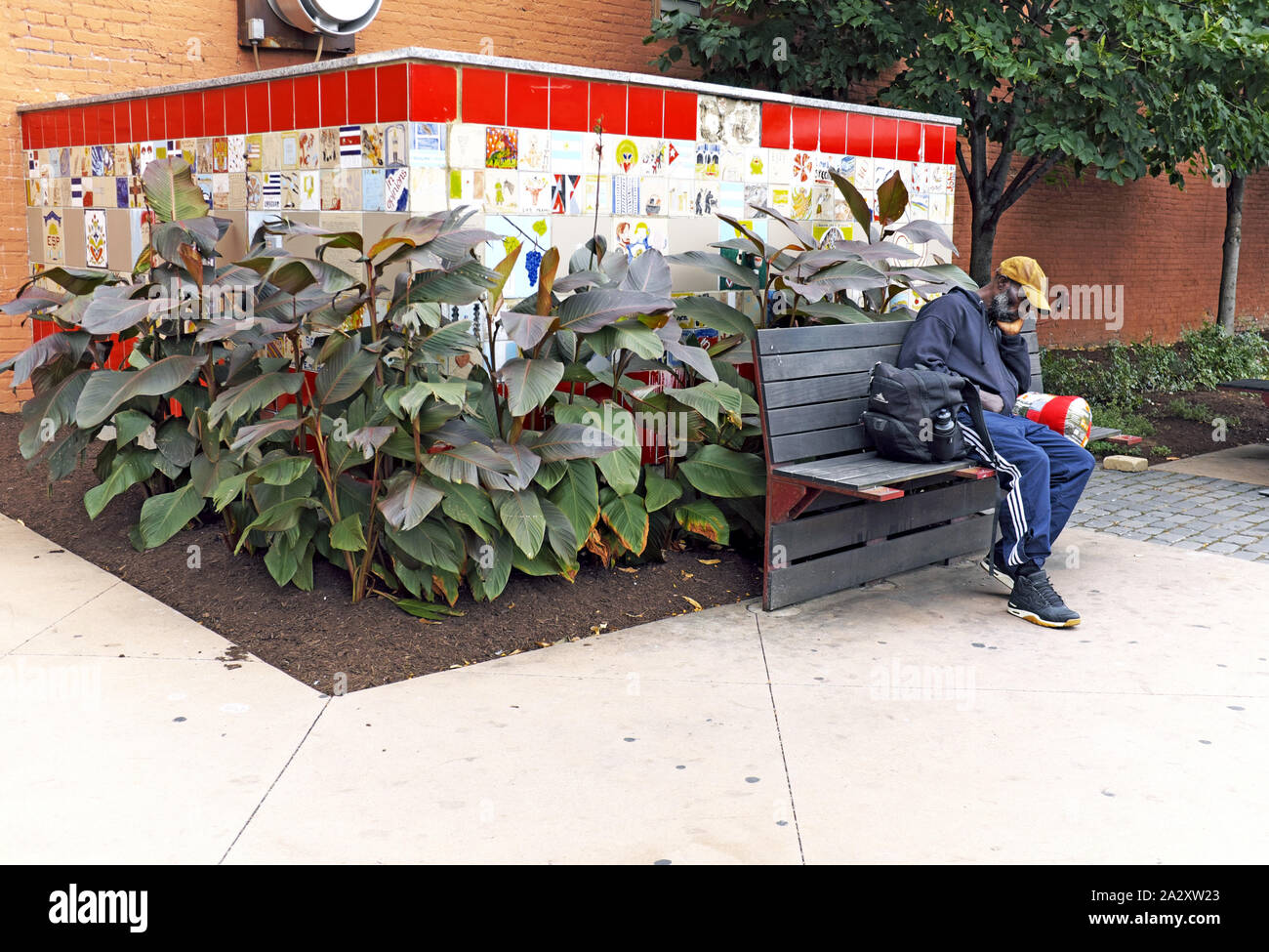 A lone black man sits on a park bench in Ohio City, a rapidly gentifying neighborhood of Cleveland, Ohio, USA. Stock Photo