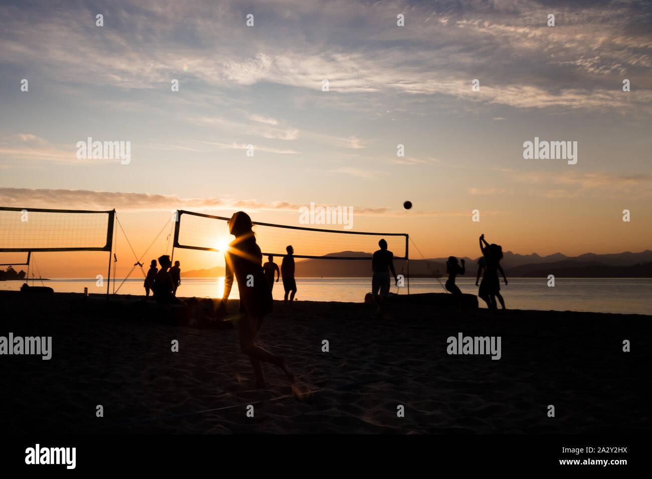 Group of young people playing beach volleyball silhouetted against the sunset at Kits Beach in Vancouver, BC. Stock Photo