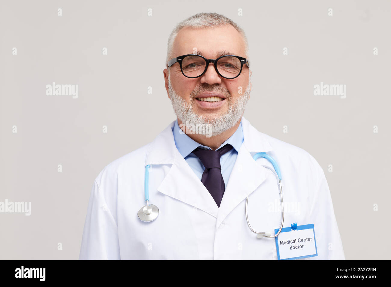Portrait of mature doctor with grey beard and grey hair in eyeglasses  smiling at camera while standing over white background Stock Photo - Alamy